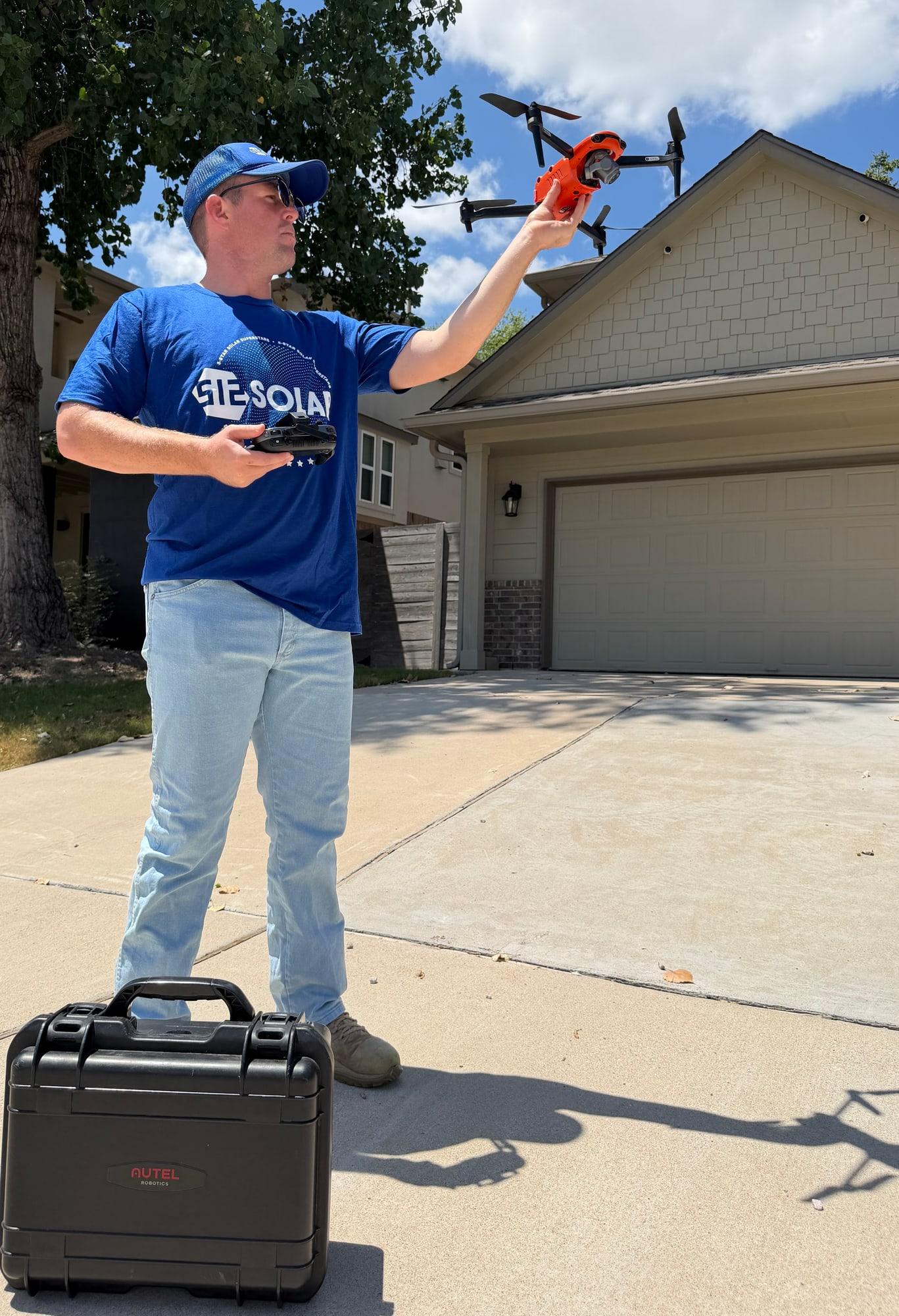 A 512 Solar technician in a branded shirt and cap launching a survey drone from a residential driveway, controller in hand and flight case at his feet
