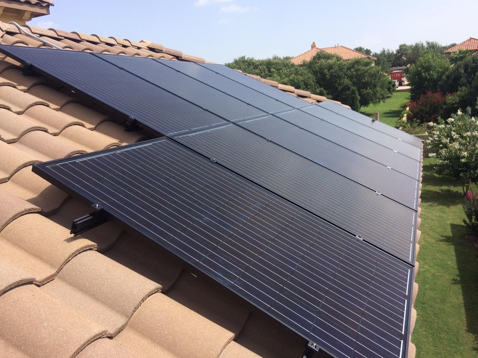 Black solar panels fitted to a tan clay tile roof, with the neighbourhood beyond