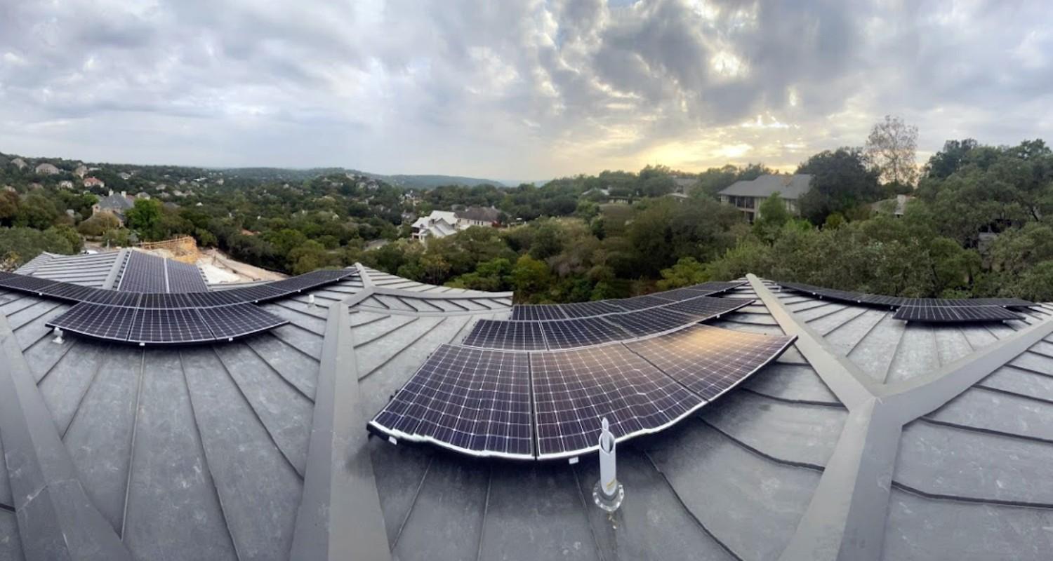 Solar panels mounted on a standing seam metal roof, with the Texas Hill Country behind it at dusk