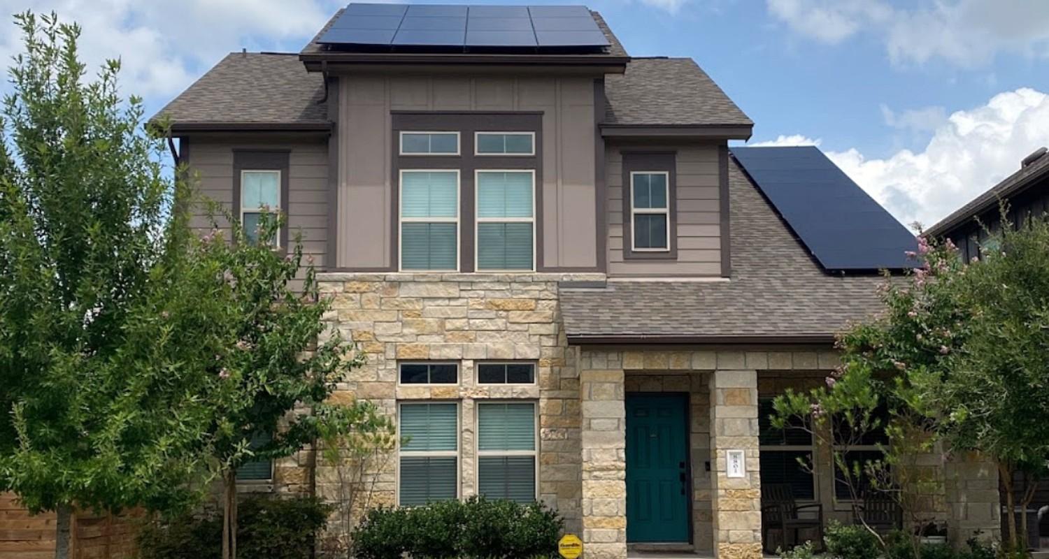 Two-story stone and siding home with all-black solar panels across two roof planes